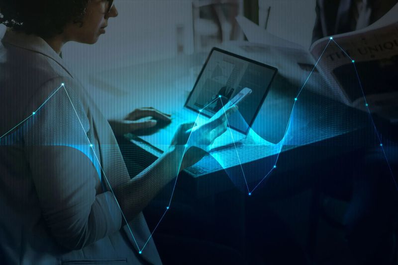 Femme travaillant sur ordinateur et tablette entourée de graphiques numériques